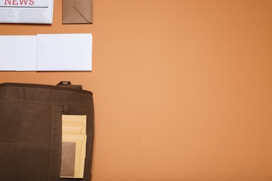 Postman bag, newspaper and mails on light brown background, flat lay. Space for text