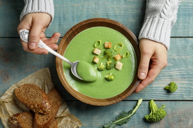 Photo of Woman eating fresh vegetable detox soup made of broccoli with croutons at table, top view