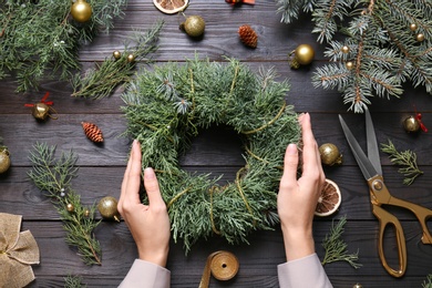 Florist with beautiful Christmas wreath of fir branches at black wooden table, top view