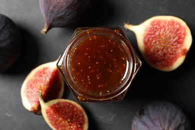 Glass jar with tasty sweet jam and fresh figs on grey textured table, flat lay