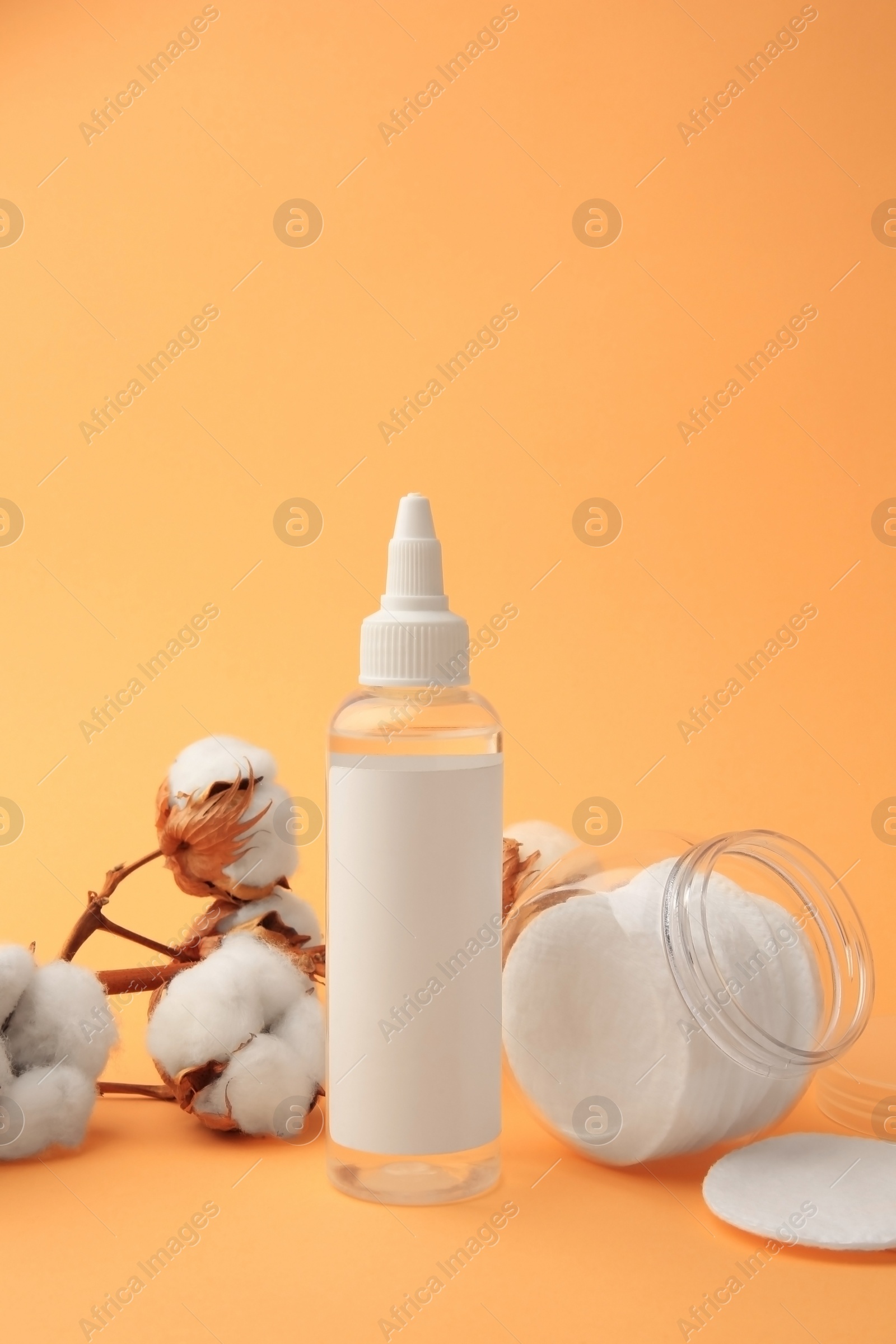 Photo of Composition with makeup remover and cotton flowers on pale orange background, space for text