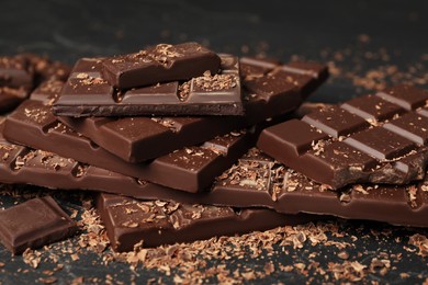 Pieces and shavings of tasty chocolate on dark table, closeup