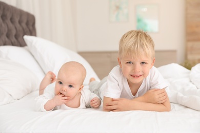 Photo of Cute boy with his little sister lying on bed at home