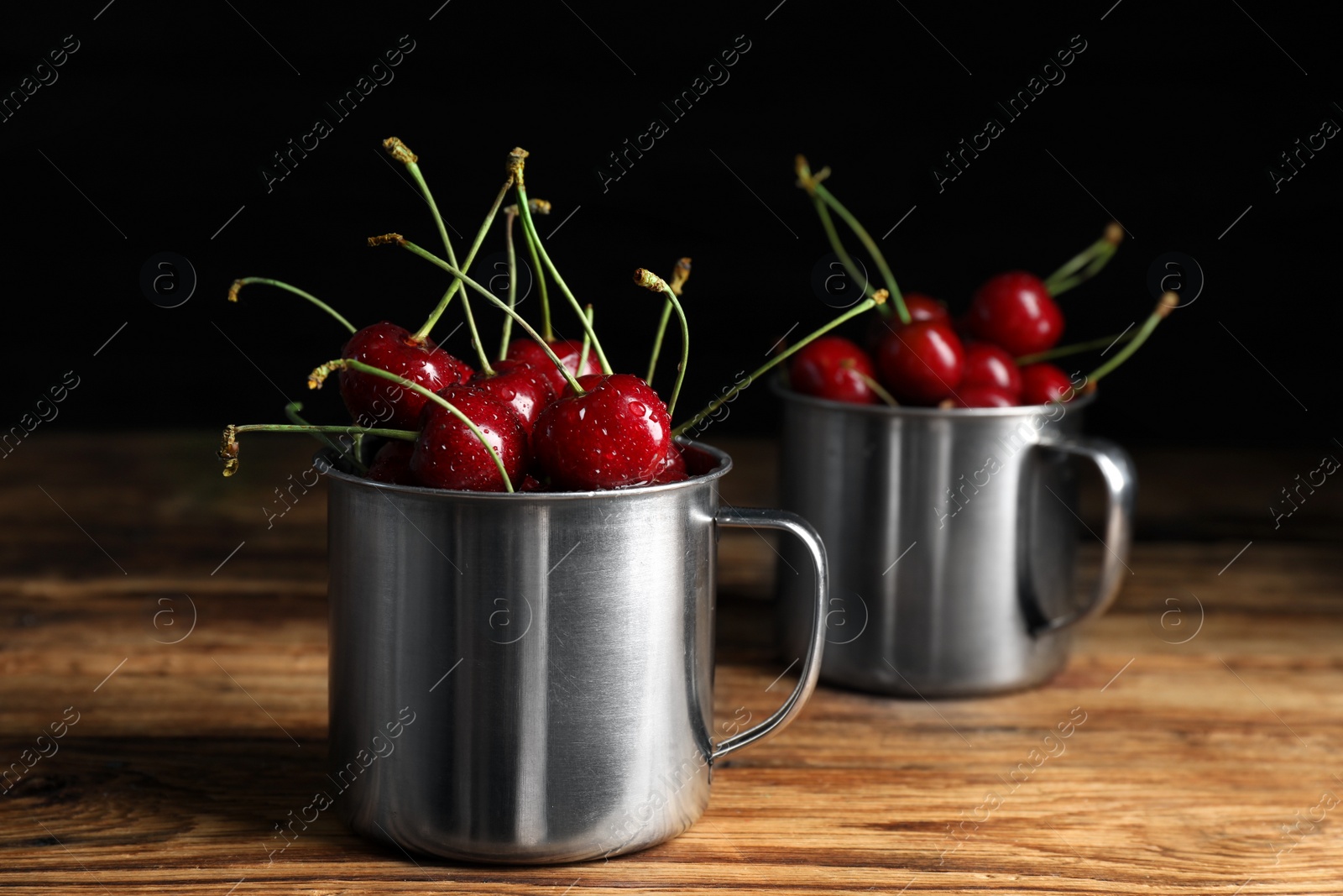 Photo of Wet red cherries in enameled mug on wooden table