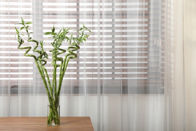 Vase with bamboo stems on wooden table indoors, space for text