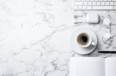 Flat lay composition with cup of coffee, earphones and stationery on white marble table