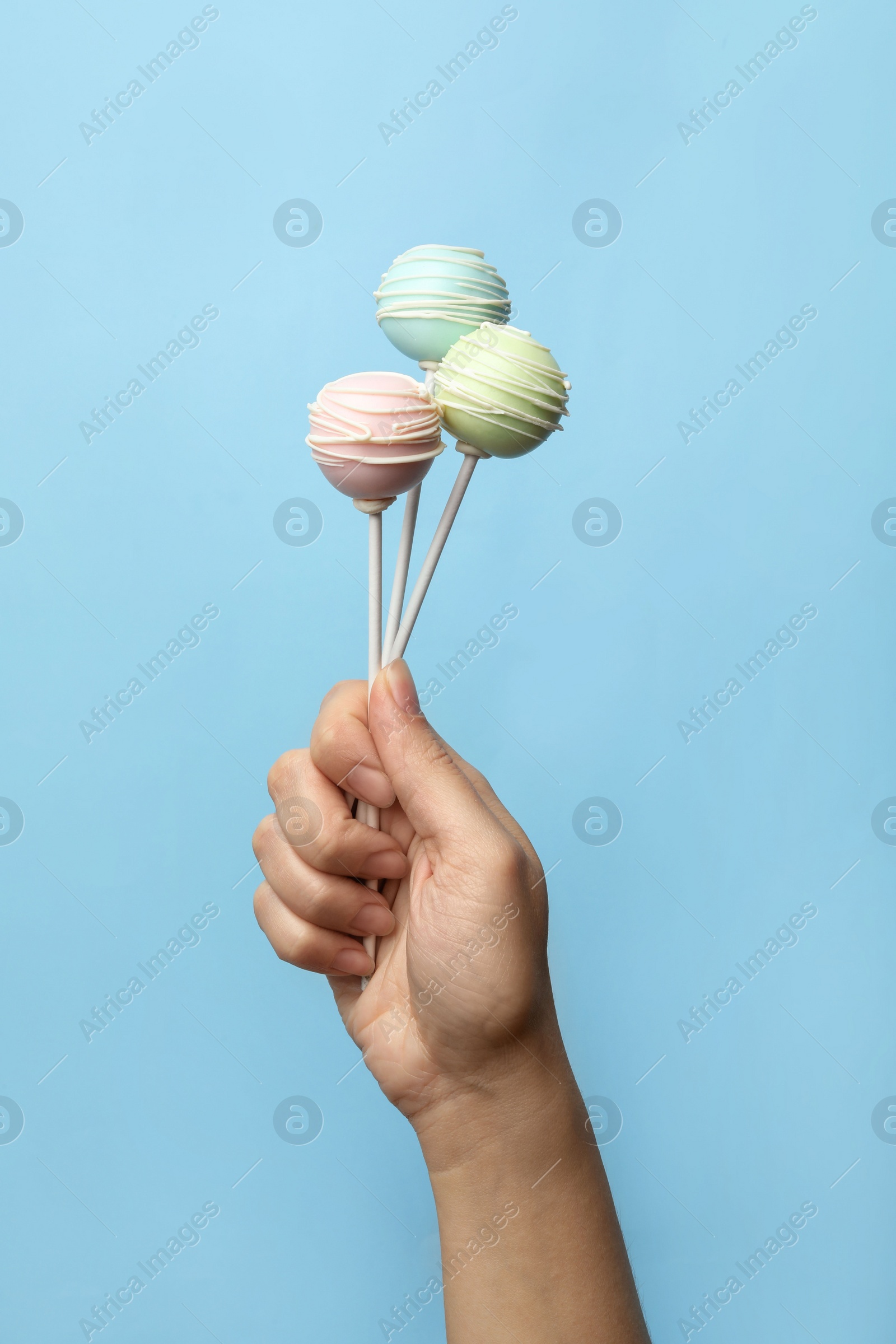 Photo of Woman holding sweet cake pops on light blue background, closeup