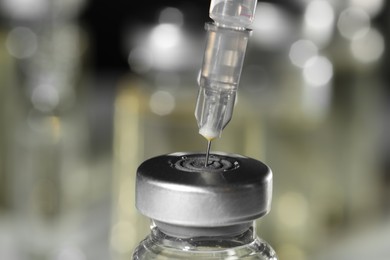 Filling syringe with medicine from vial against blurred background, closeup