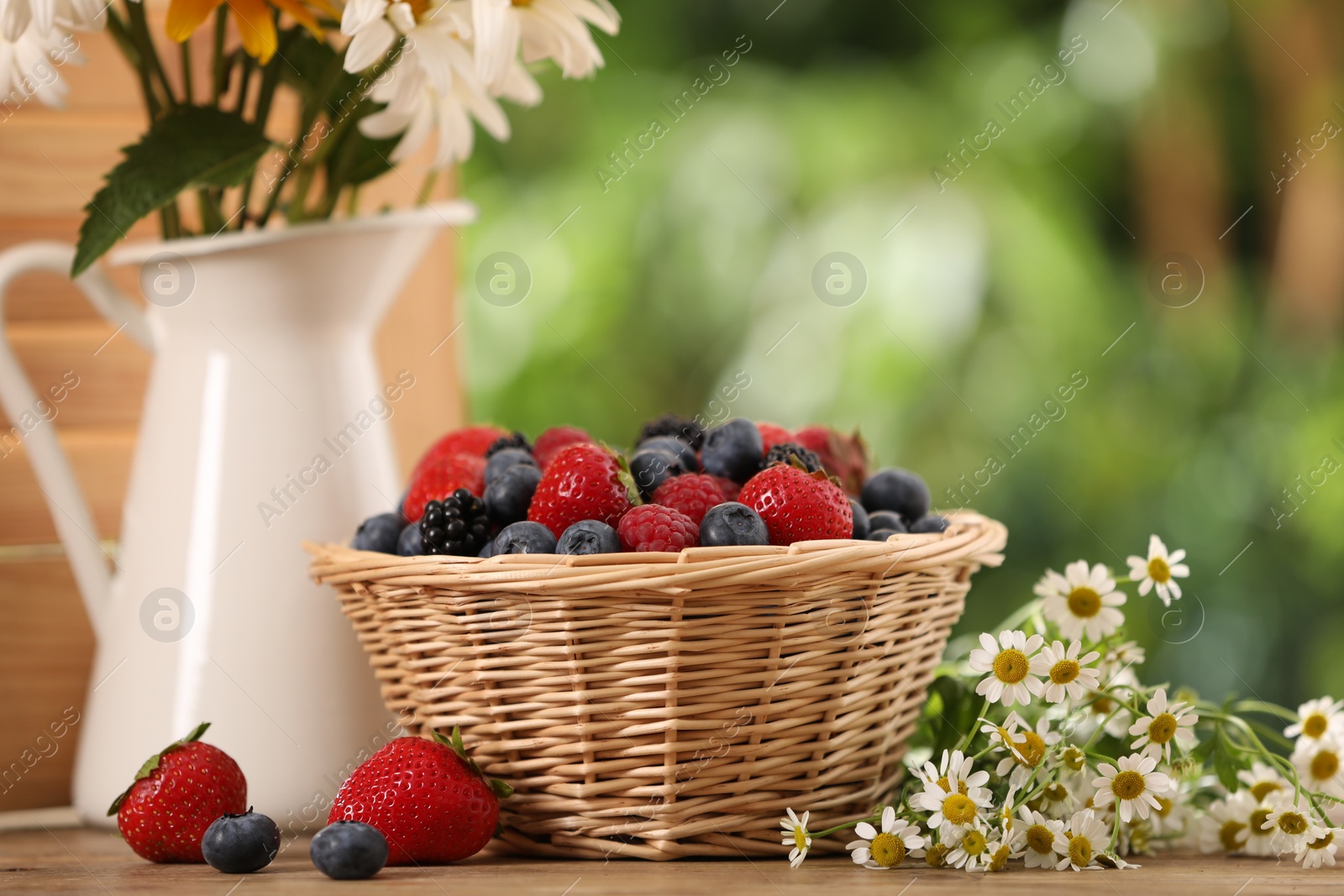 Photo of Wicker bowl with different fresh ripe berries and beautiful flowers on wooden table outdoors