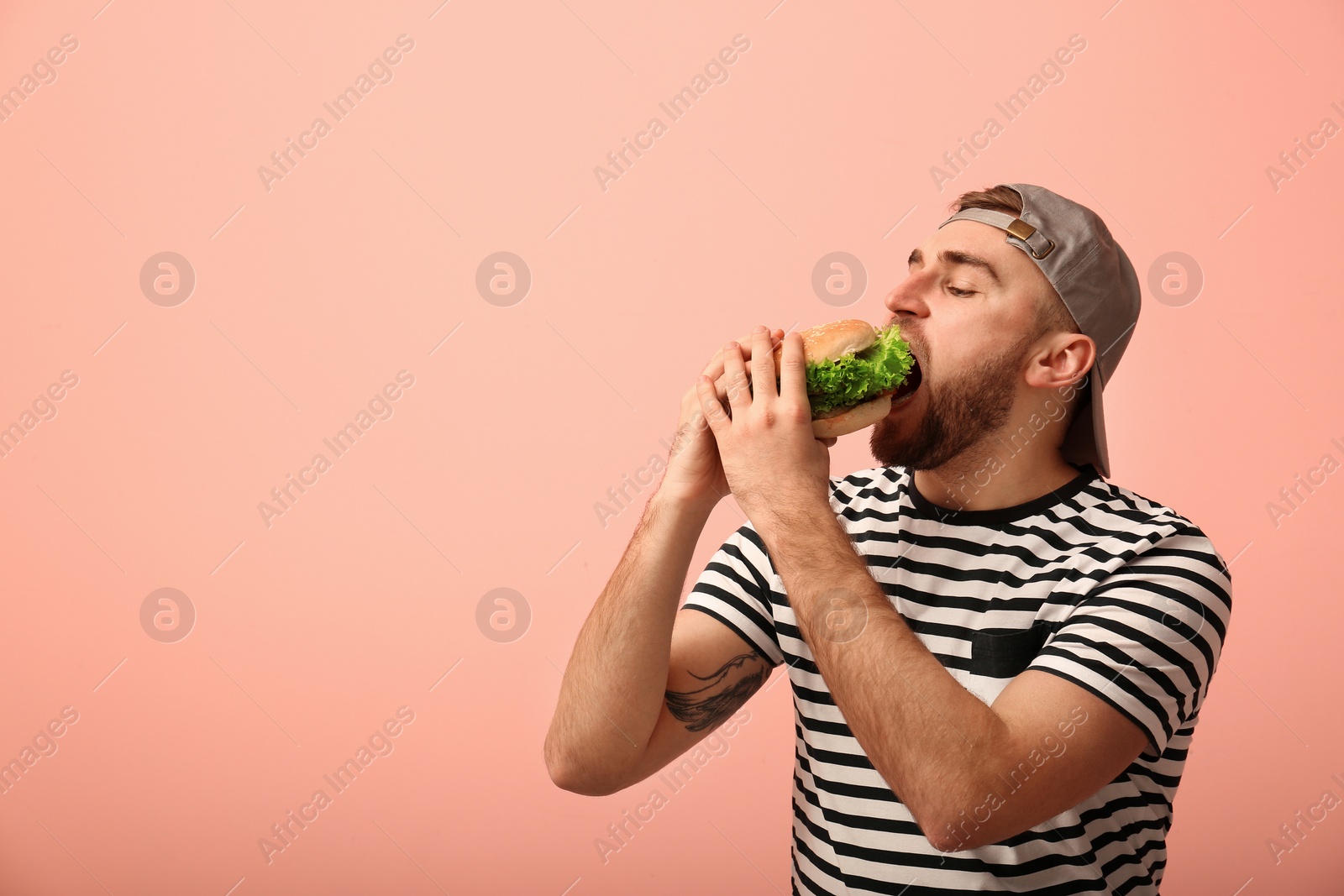 Photo of Young man eating tasty burger on color background. Space for text