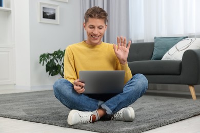 Photo of Happy young man having video chat via laptop on carpet indoors