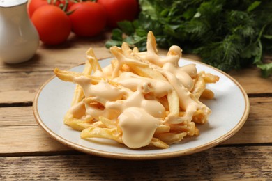 Photo of Delicious French fries with cheese sauce, tomatoes, dill and parsley on wooden table, closeup