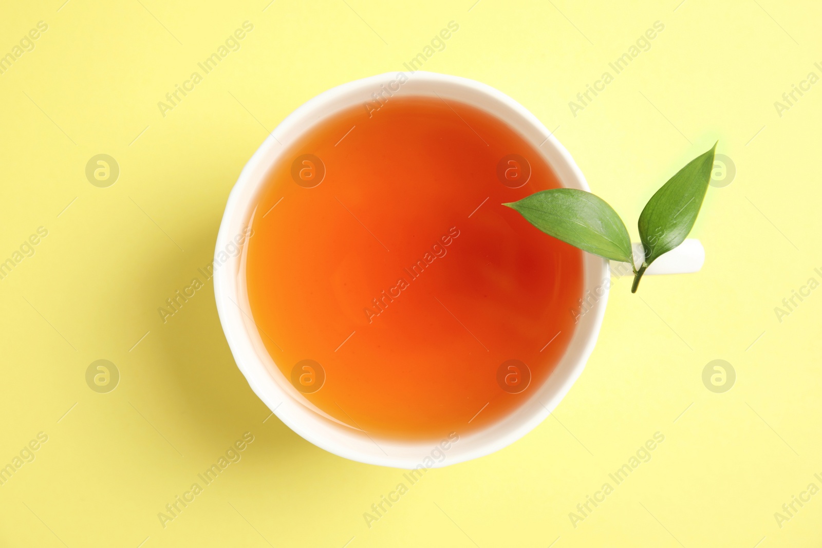 Photo of Cup of delicious tea with green leaves on color background, top view