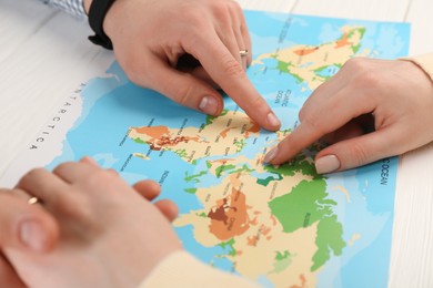 Man and woman planning their honeymoon trip with world map at white wooden table, closeup