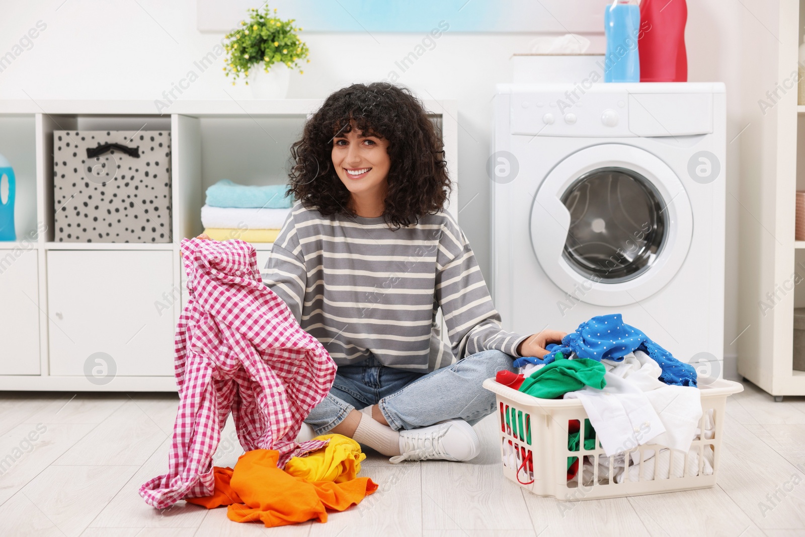 Photo of Happy woman with laundry near washing machine indoors