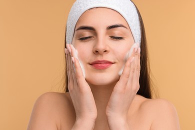 Photo of Young woman with headband washing her face on beige background