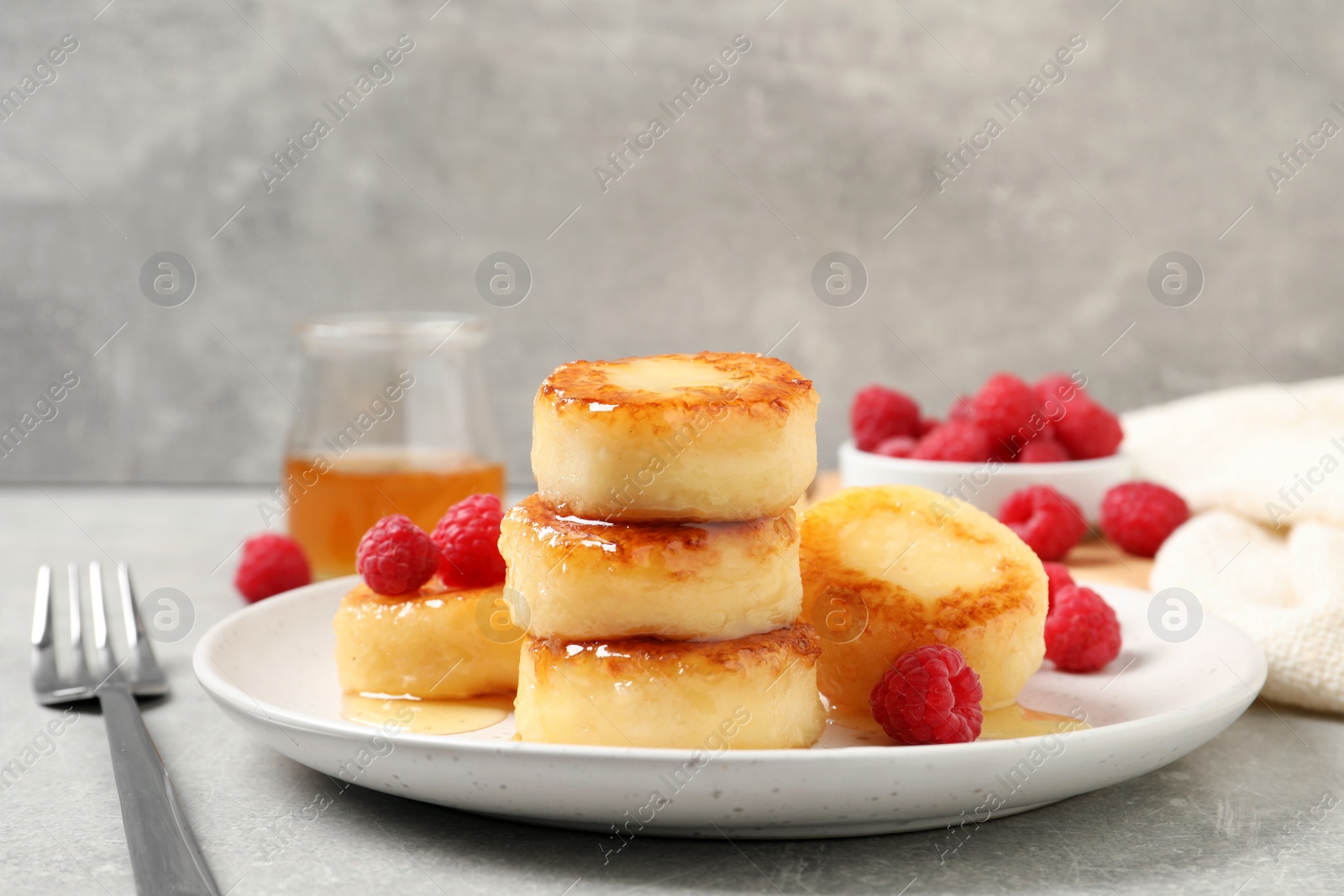 Photo of Delicious cottage cheese pancakes with raspberries and honey on light grey table