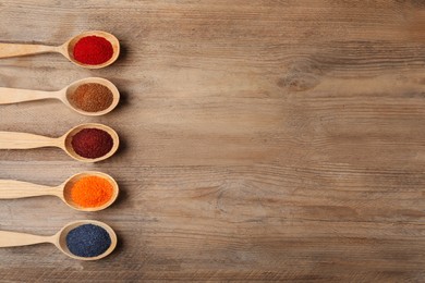 Many spoons with food coloring on wooden table, flat lay. Space for text