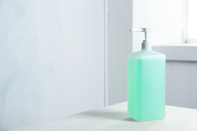Photo of Dispenser bottle with green antiseptic gel on table indoors. Space for text