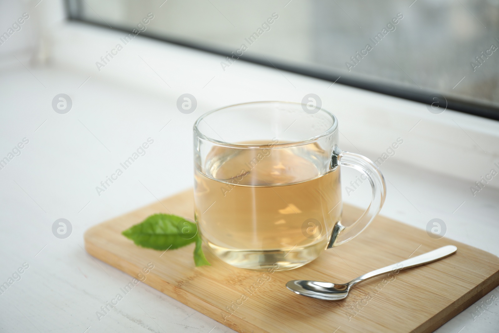 Photo of Tasty hot green tea in cup on window sill