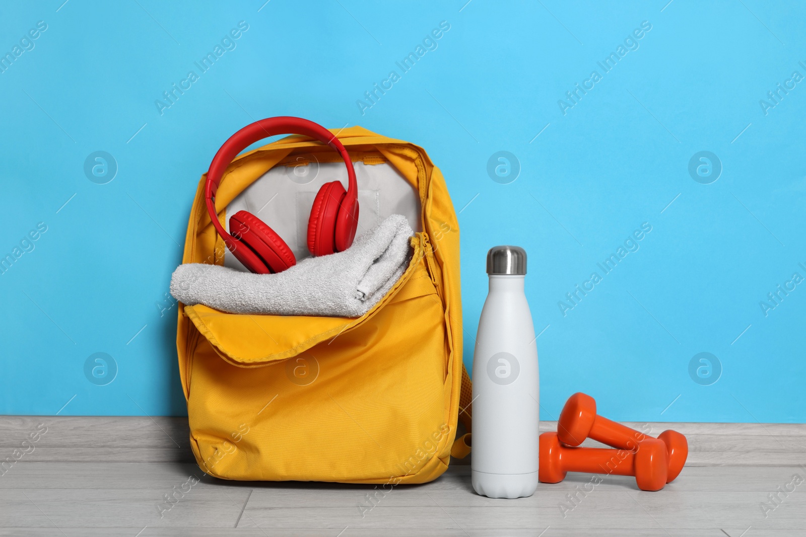 Photo of Backpack and sports equipment on floor near light blue wall