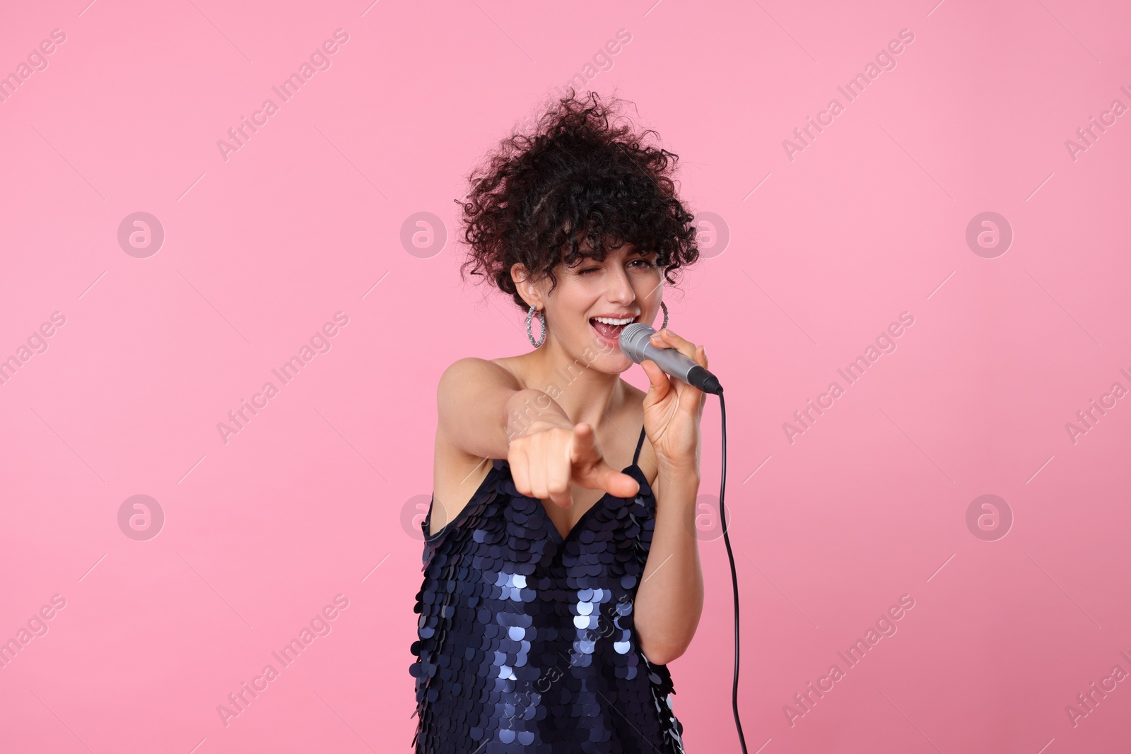 Photo of Beautiful young woman with microphone singing on pink background