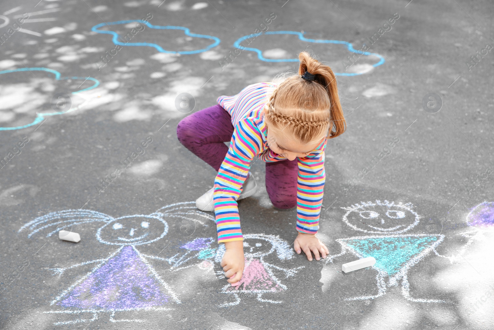 Photo of Little child drawing with colorful chalk on asphalt