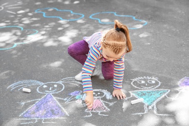 Little child drawing with colorful chalk on asphalt