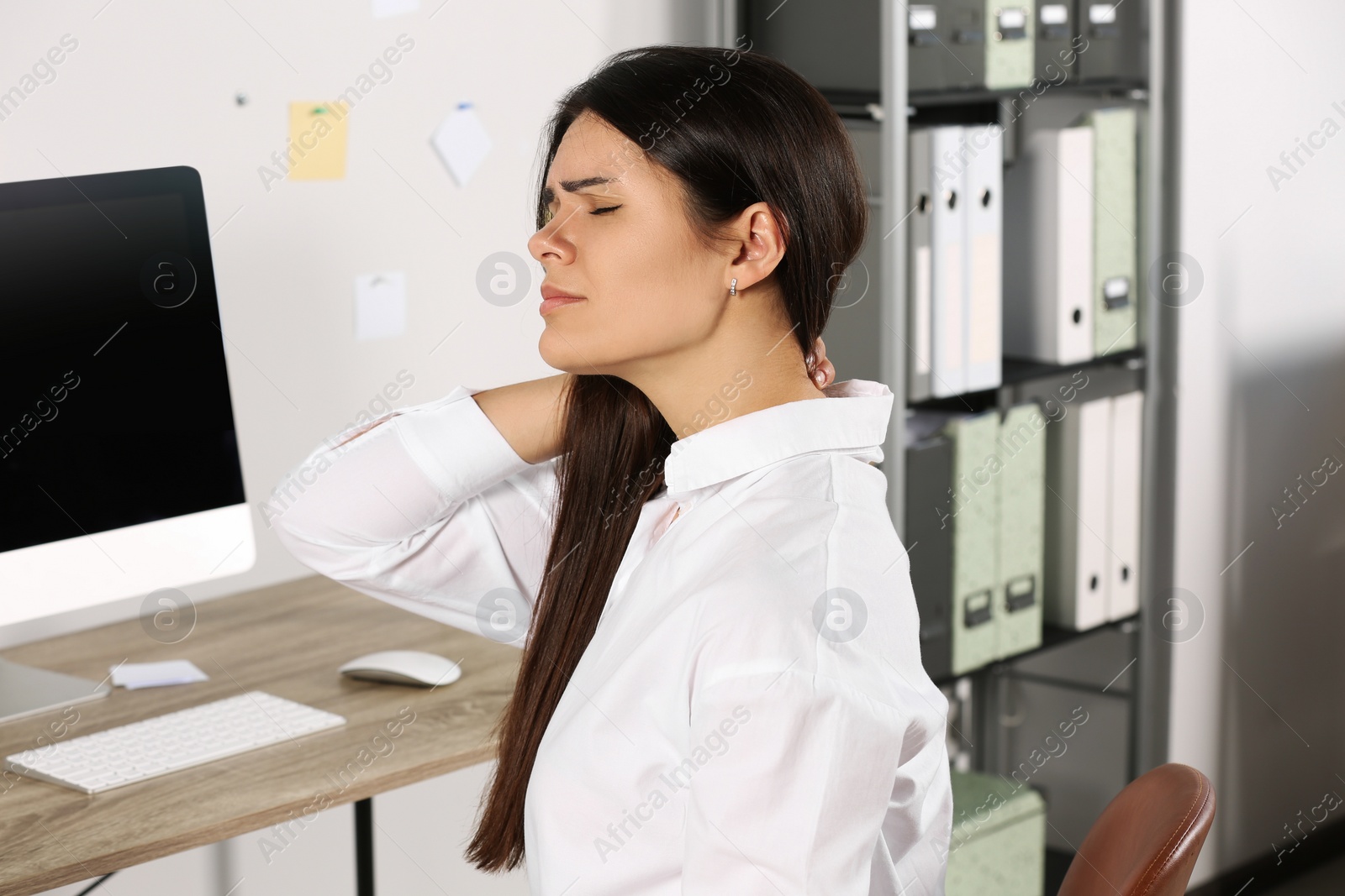 Photo of Young woman suffering from neck pain in office