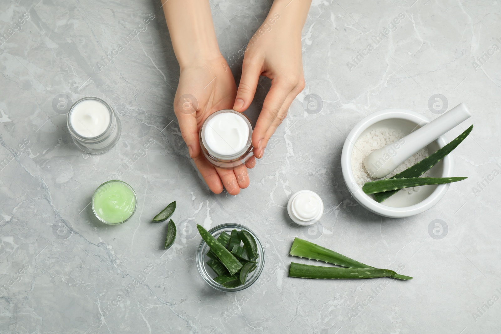 Photo of Woman with different cosmetic products and aloe at grey marble table, flat lay