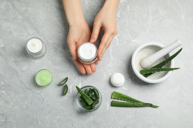 Woman with different cosmetic products and aloe at grey marble table, flat lay