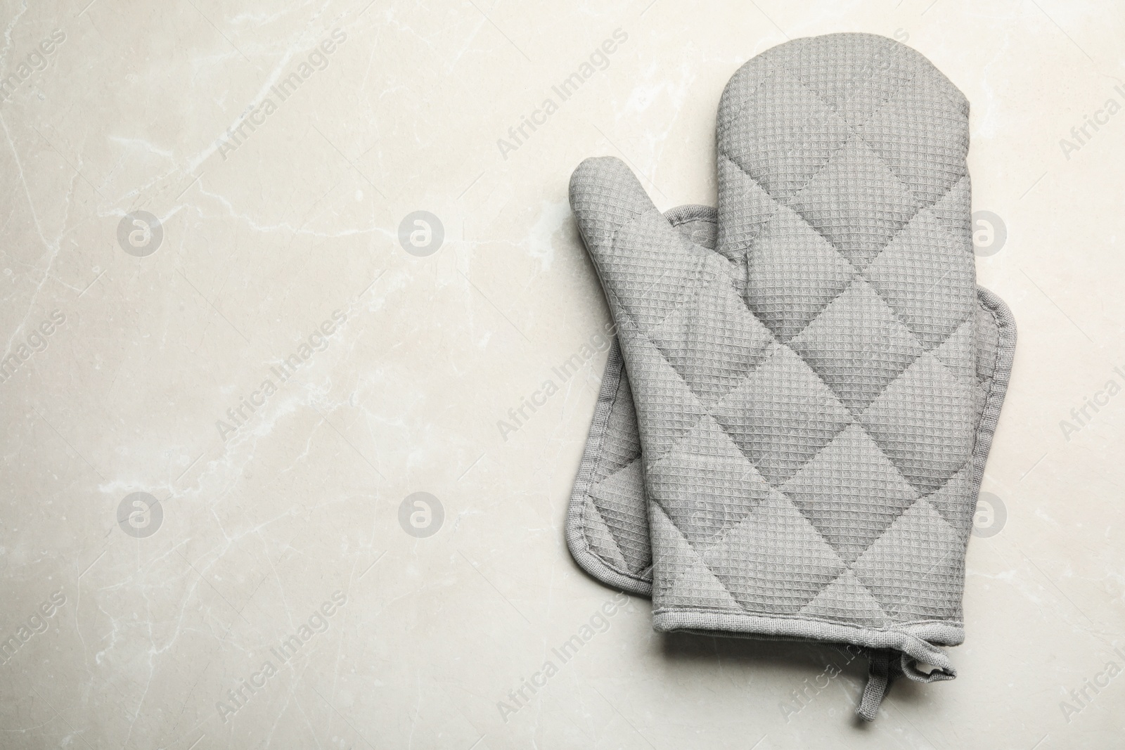 Photo of Oven mitt, pot holder and space for text on light stone background, flat lay