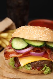 Photo of Tasty burger with bacon, vegetables and patty on parchment paper, closeup