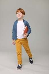 Happy schoolboy with books on grey background