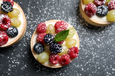 Delicious tartlets with berries on black table, flat lay