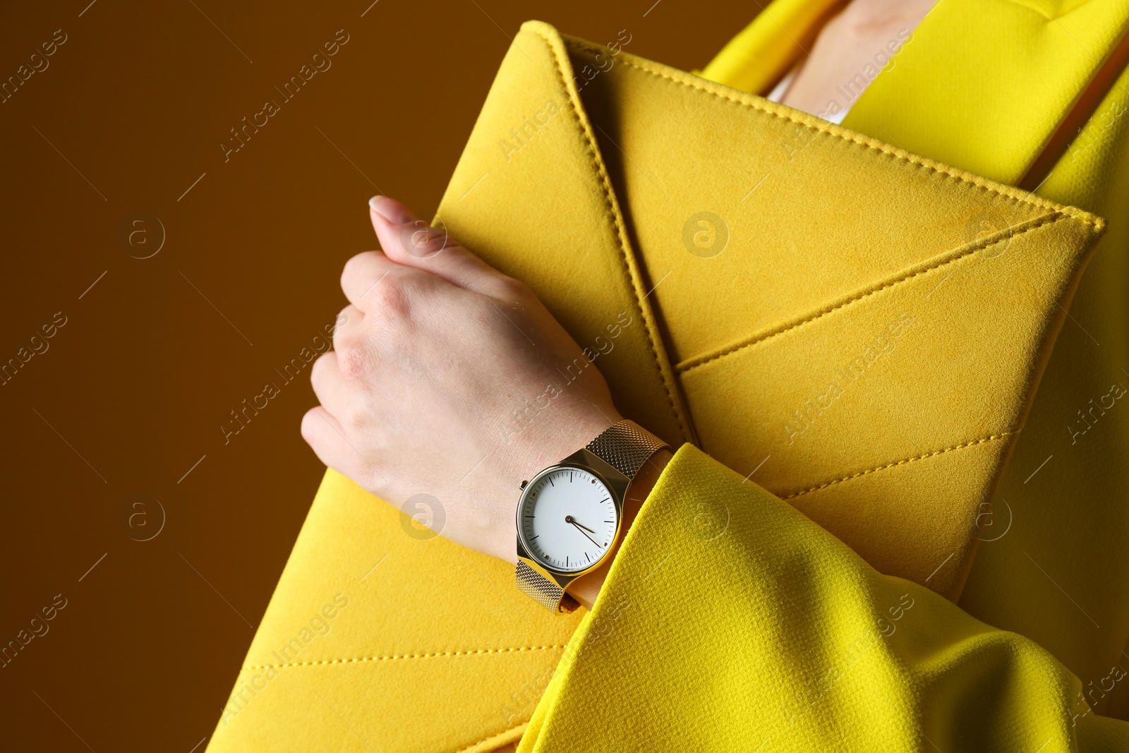 Photo of Woman wearing luxury wristwatch on brown background, closeup