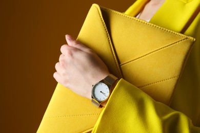 Photo of Woman wearing luxury wristwatch on brown background, closeup