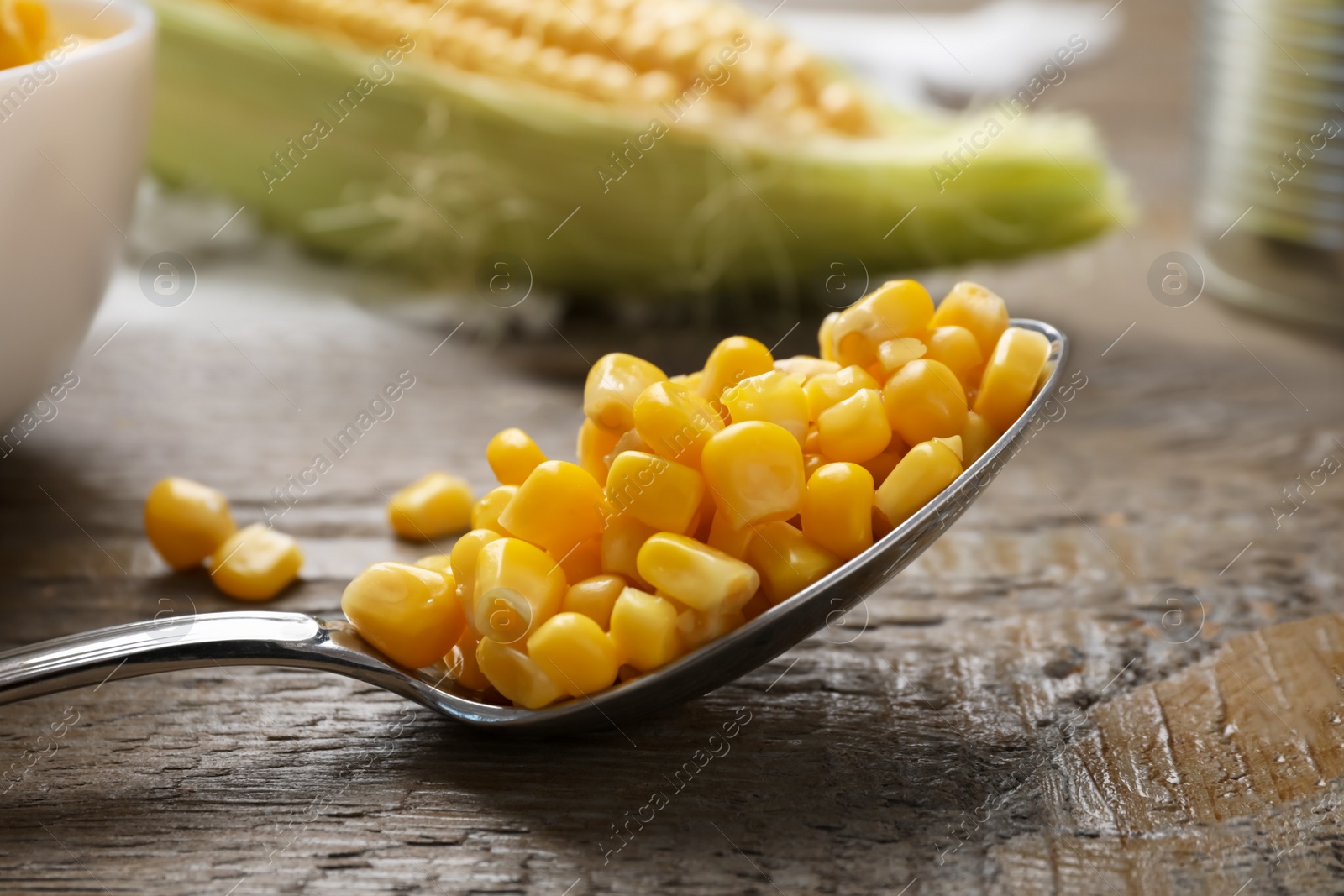 Photo of Spoon of preserved corn on wooden table, closeup