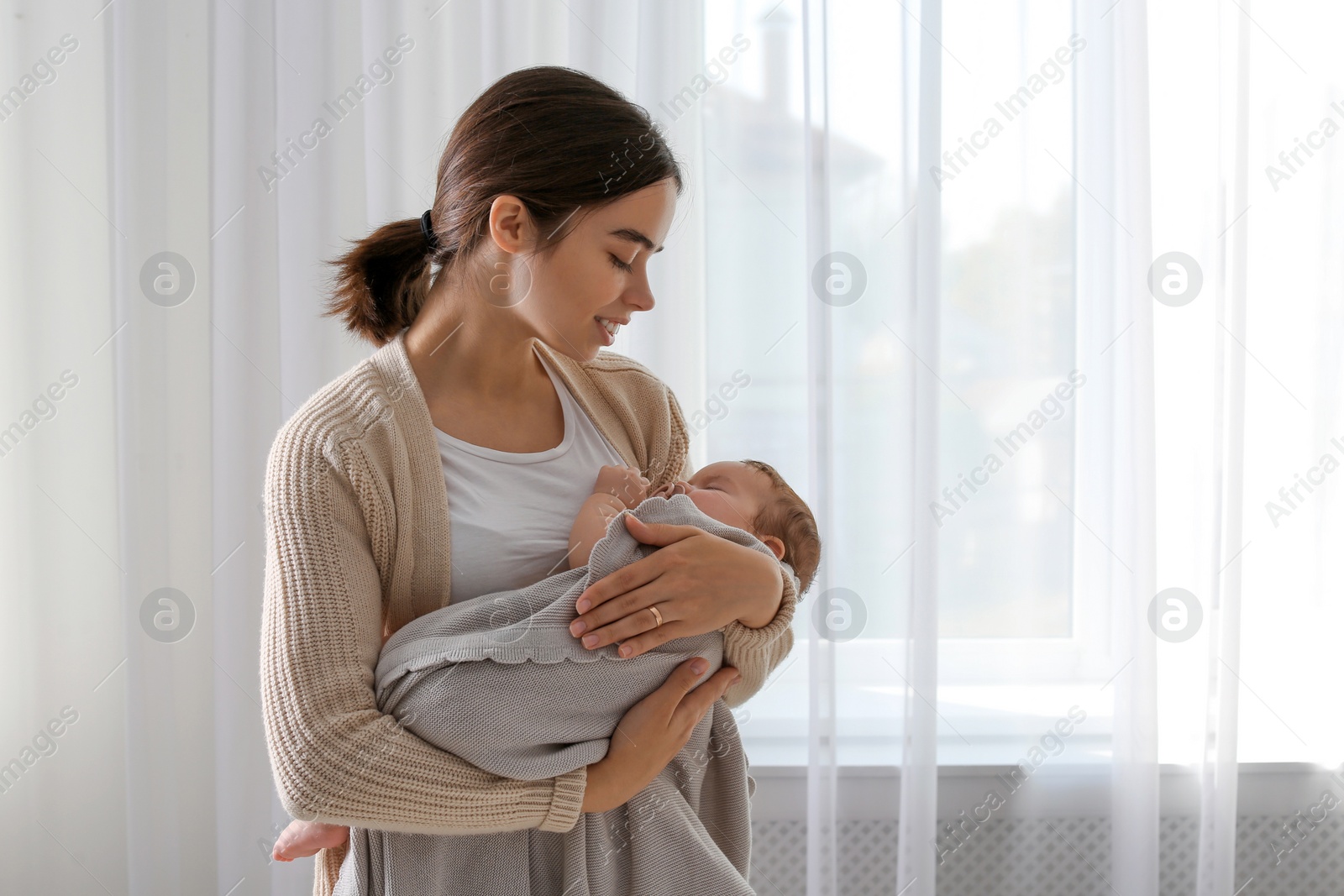 Photo of Young woman with her little baby near window at home