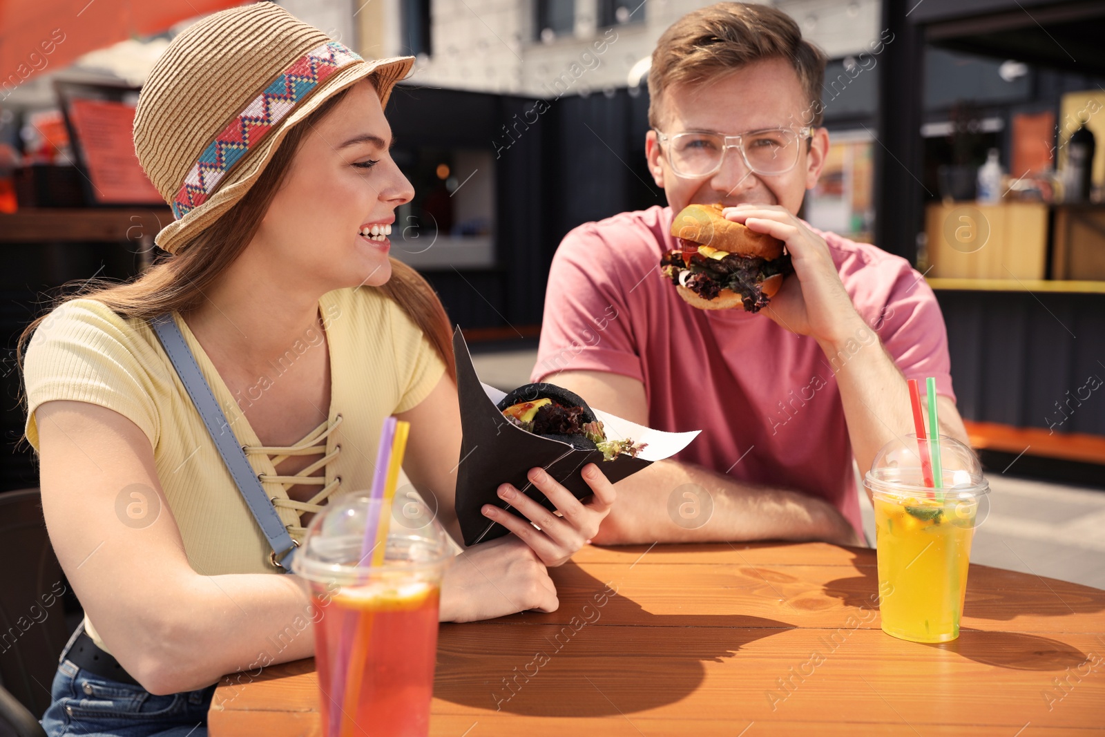 Photo of Young happy couple with burgers in street cafe