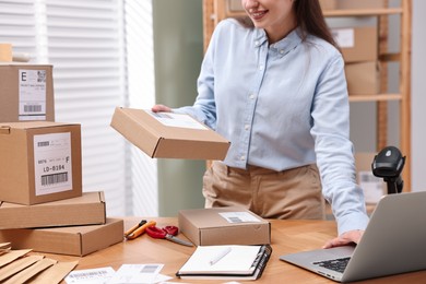 Photo of Parcel packing. Post office worker using laptop at wooden table indoors, closeup