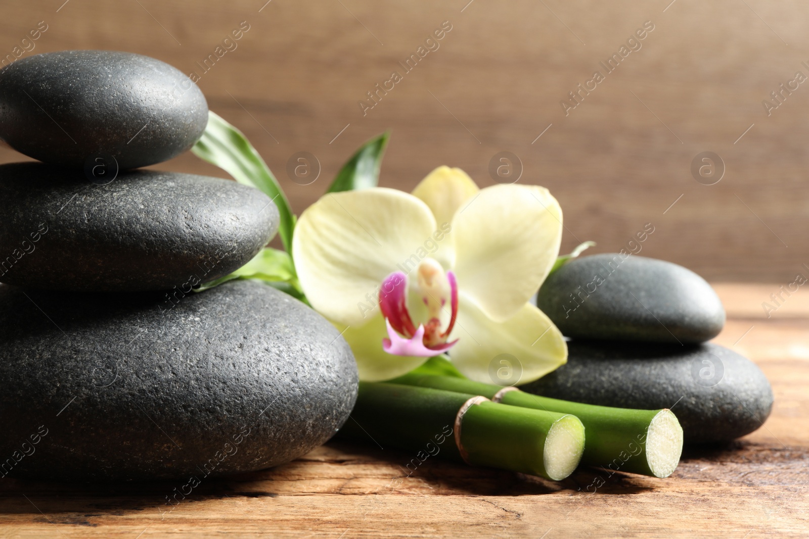 Photo of Spa stones, bamboo stems and beautiful orchid flower on wooden table, closeup