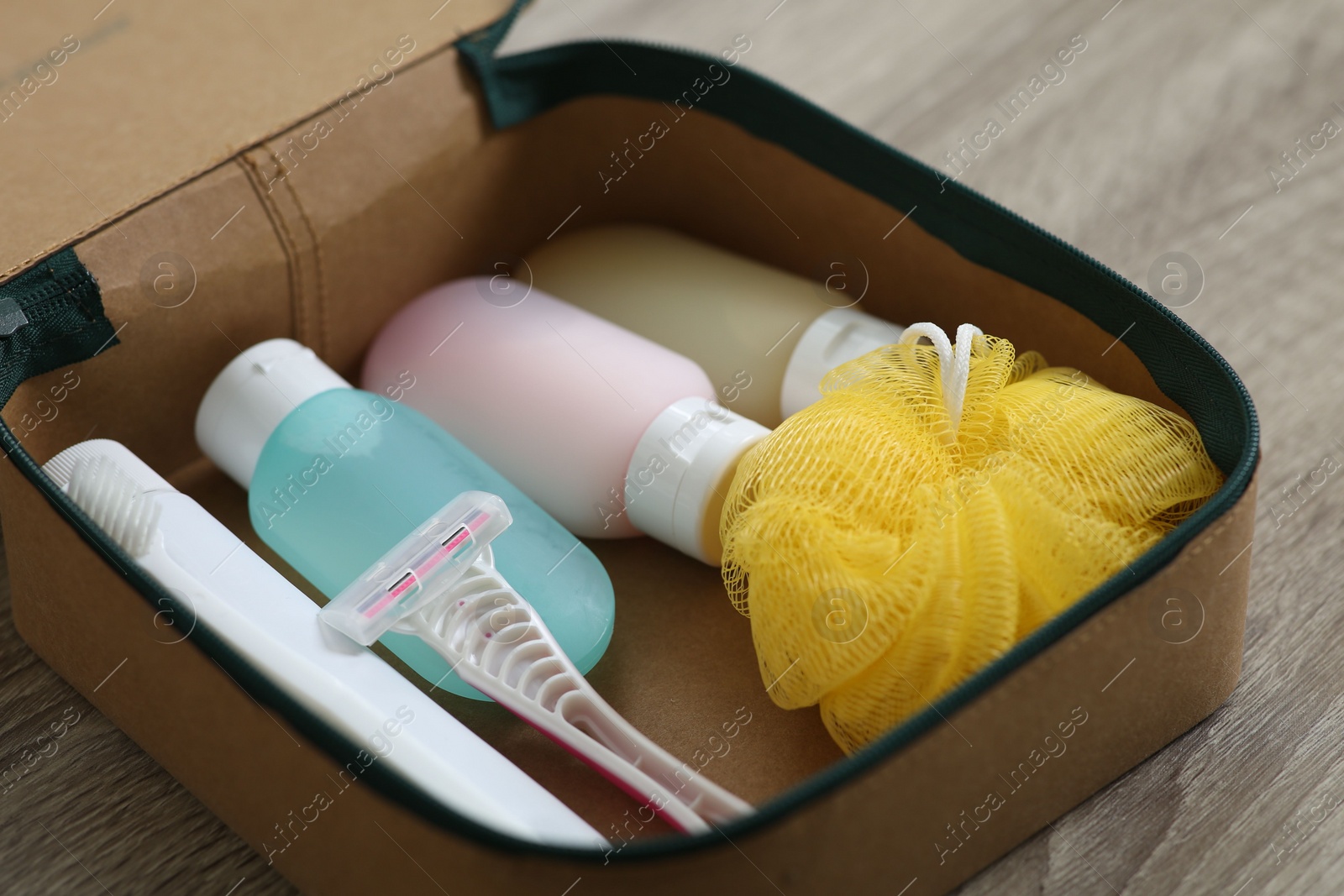 Photo of Cosmetic travel kit in compact toiletry bag on wooden table, closeup. Bath accessories