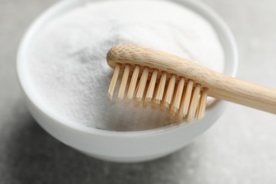 Bamboo toothbrush and bowl of baking soda on grey table, closeup