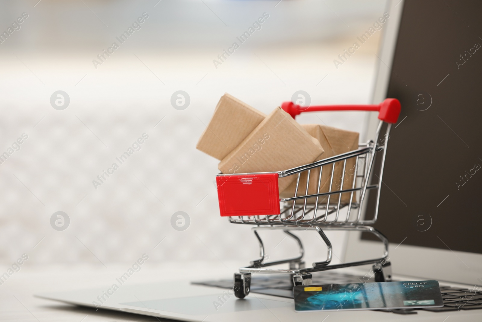 Photo of Online payment concept. Small shopping cart with bank card, boxes and laptop on table, space for text