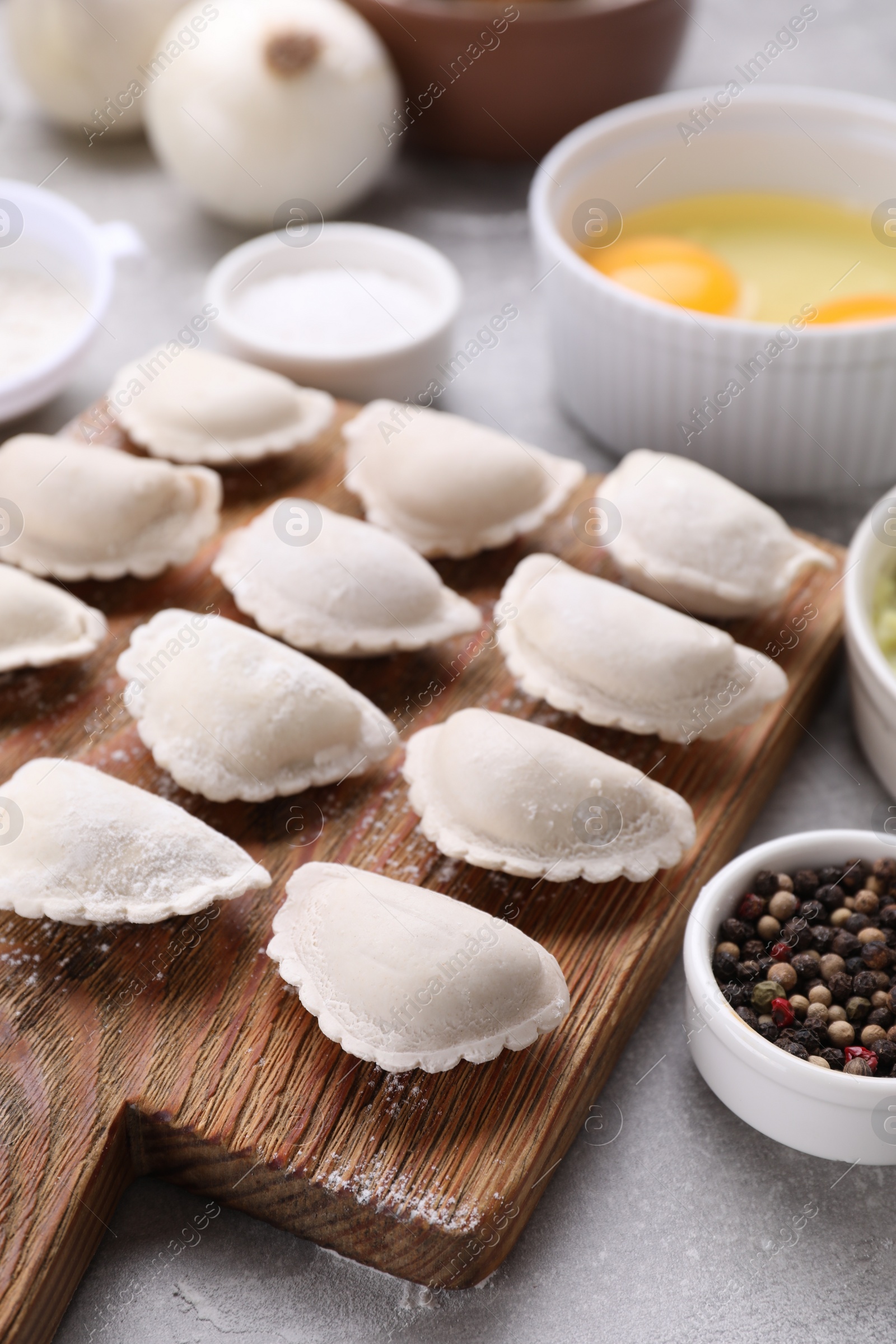 Photo of Raw dumplings (varenyky) and ingredients on grey table