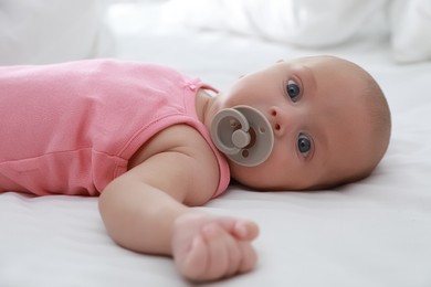 Photo of Cute little baby with pacifier lying on bed, closeup