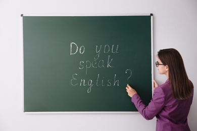 Photo of Teacher near green chalkboard with words Do You Speak English?