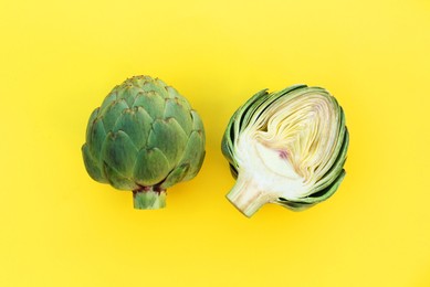 Photo of Whole and cut fresh raw artichokes on pale yellow background, flat lay