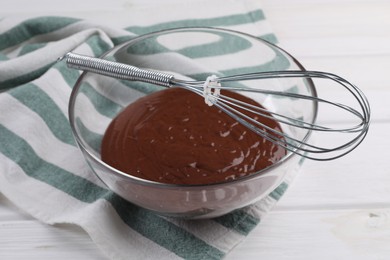 Photo of Bowl of chocolate cream and whisk on white wooden table, closeup